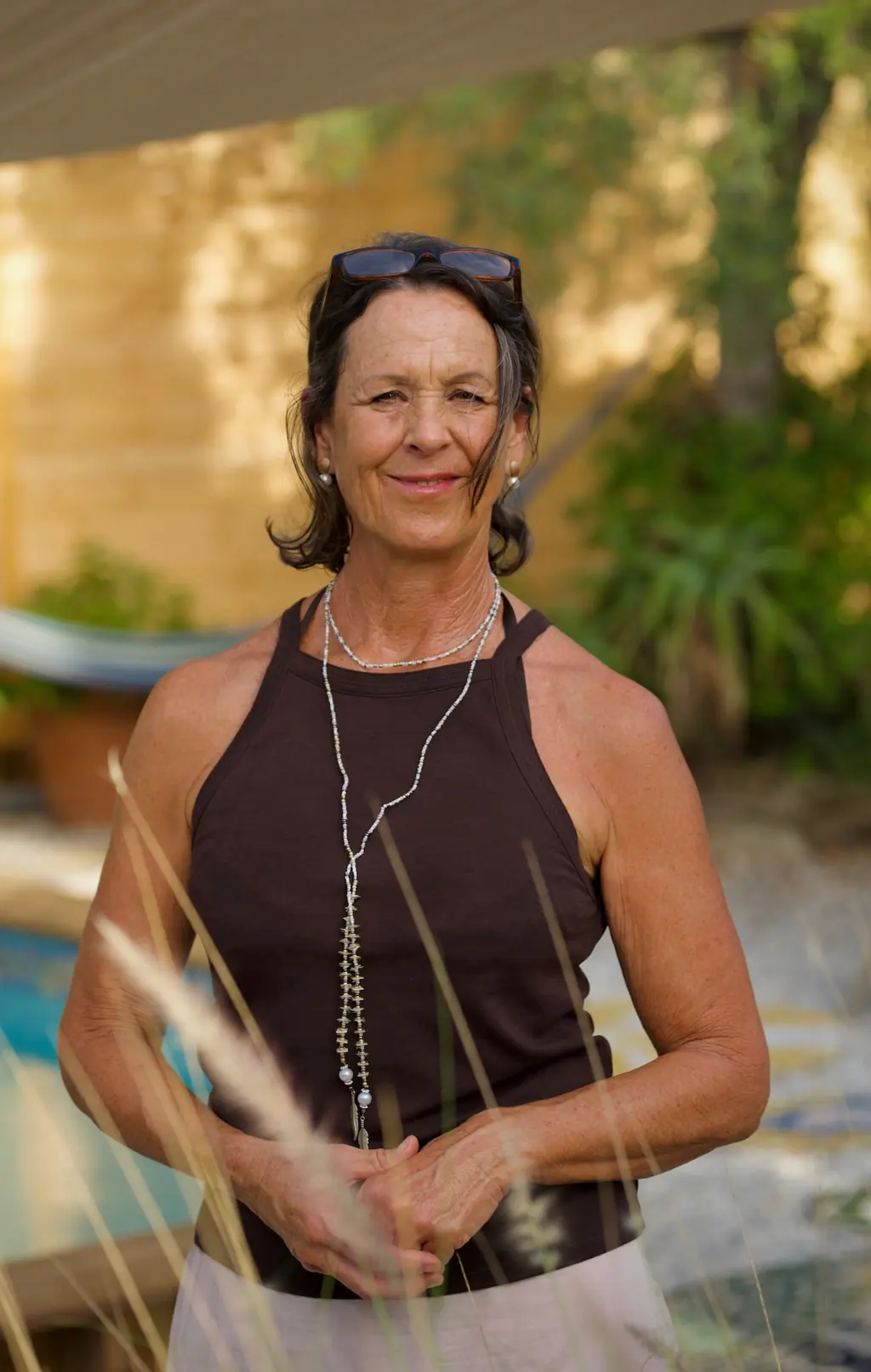 Darja Quitsch lächelnd im sonnigen Garten, die Hände locker ineinandergelegt, im Vordergrund Gräser